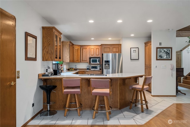 kitchen with appliances with stainless steel finishes, a kitchen breakfast bar, light hardwood / wood-style floors, and kitchen peninsula