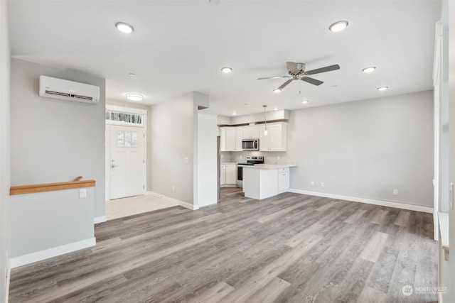 unfurnished living room with a wall unit AC, ceiling fan, and light hardwood / wood-style flooring