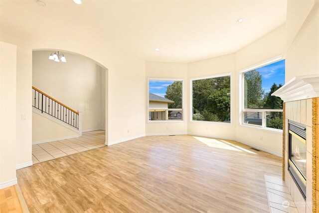 unfurnished living room with plenty of natural light, a tiled fireplace, light hardwood / wood-style floors, and a chandelier