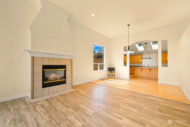 unfurnished living room featuring a fireplace, a notable chandelier, wood-type flooring, sink, and high vaulted ceiling