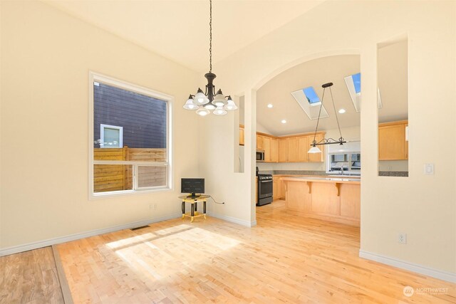 interior space featuring hanging light fixtures, lofted ceiling with skylight, light hardwood / wood-style floors, and a breakfast bar