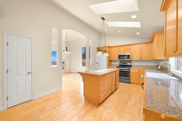 kitchen featuring a skylight, light wood-style flooring, appliances with stainless steel finishes, a center island, and a sink