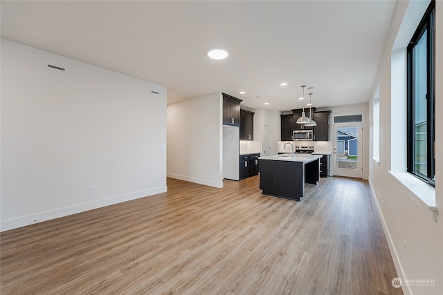 kitchen featuring a center island with sink, white refrigerator, decorative light fixtures, sink, and light hardwood / wood-style flooring