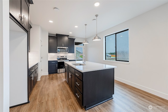 kitchen with a kitchen island with sink, appliances with stainless steel finishes, decorative light fixtures, sink, and light hardwood / wood-style flooring