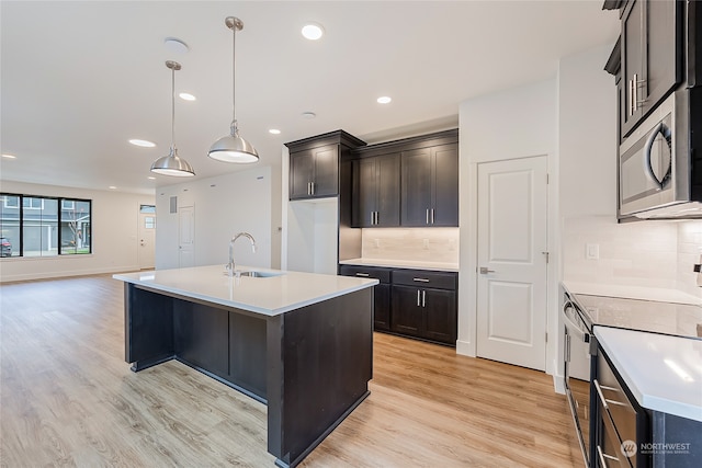 kitchen featuring a center island with sink, stainless steel appliances, light wood-type flooring, hanging light fixtures, and sink