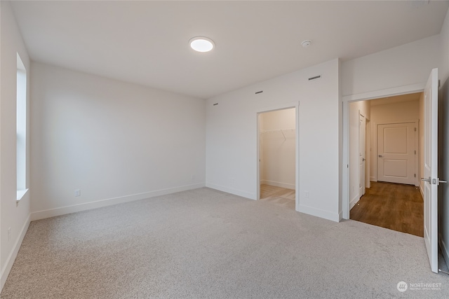 unfurnished bedroom with light colored carpet, a closet, and a spacious closet