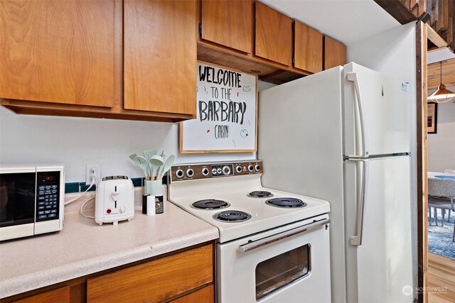 kitchen featuring light countertops, white appliances, brown cabinetry, and decorative light fixtures