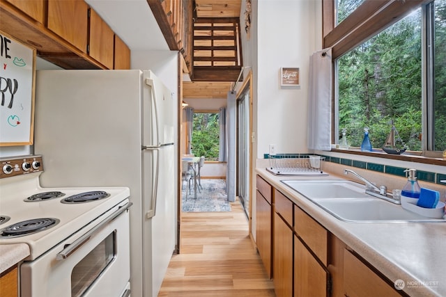 kitchen with light wood-style flooring, brown cabinets, light countertops, white electric range, and a sink