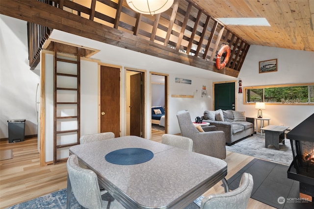 dining area featuring wooden ceiling, light wood-style flooring, a skylight, and high vaulted ceiling