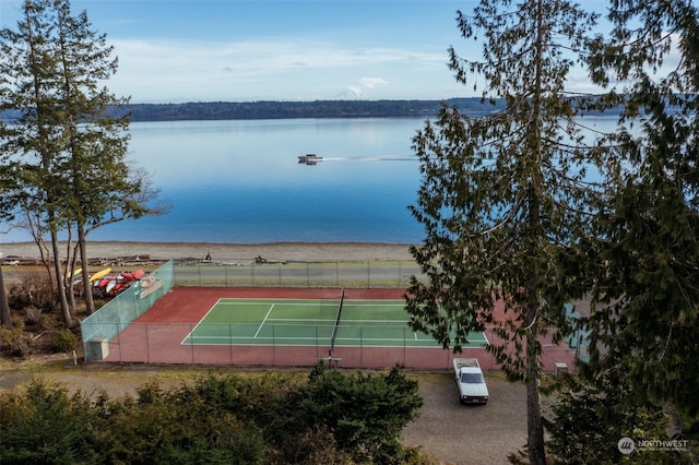 view of tennis court with a water view and fence