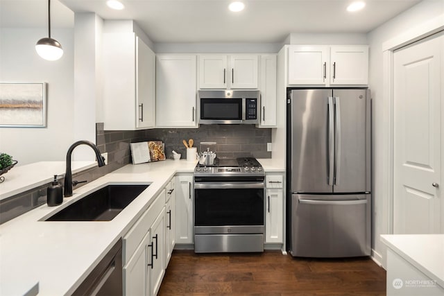 kitchen featuring pendant lighting, dark wood-type flooring, stainless steel appliances, sink, and white cabinetry