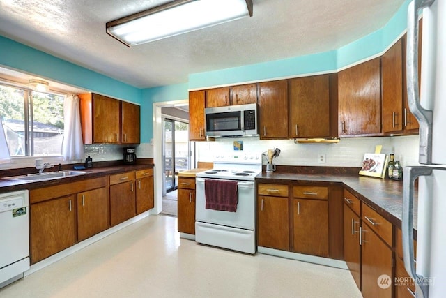 kitchen featuring white appliances, backsplash, dark countertops, and a sink