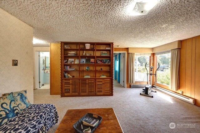 sitting room with a textured ceiling, baseboard heating, wooden walls, and carpet