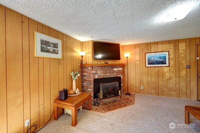 carpeted living room featuring a textured ceiling, wood walls, and a fireplace