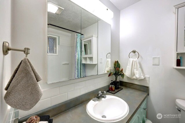 bathroom with toilet, vanity, a textured ceiling, tasteful backsplash, and curtained shower