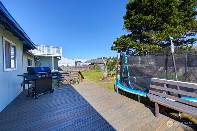 wooden deck featuring a trampoline, a lawn, and area for grilling