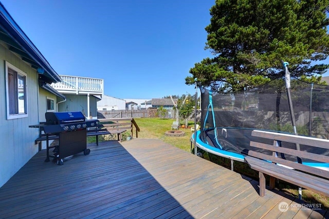 wooden terrace with a trampoline, a fenced backyard, a grill, and a lawn