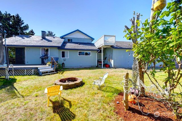 rear view of house with a lawn, a fire pit, and a deck