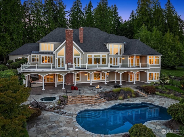 back of property at dusk with a patio, french doors, a chimney, and a balcony