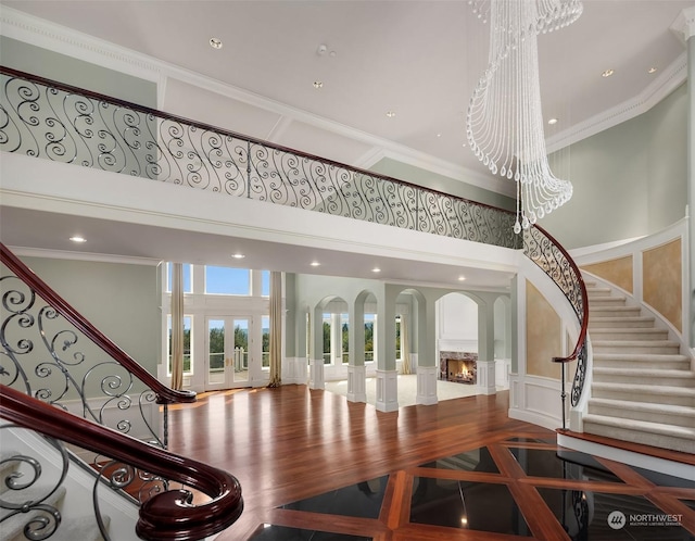 foyer entrance featuring arched walkways, a decorative wall, a towering ceiling, stairs, and ornamental molding