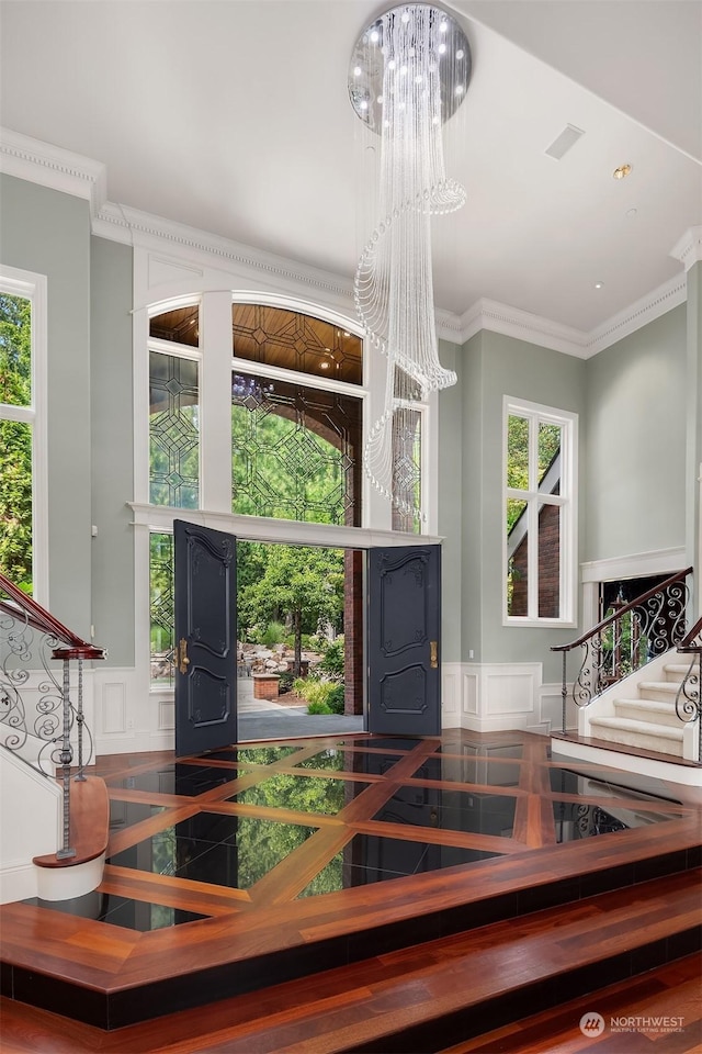 entrance foyer featuring a wainscoted wall, stairs, ornamental molding, and a decorative wall