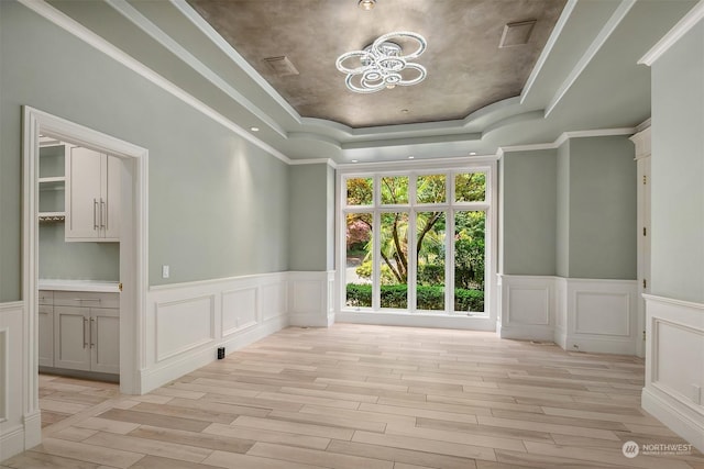 empty room featuring light wood finished floors, a tray ceiling, visible vents, and a decorative wall