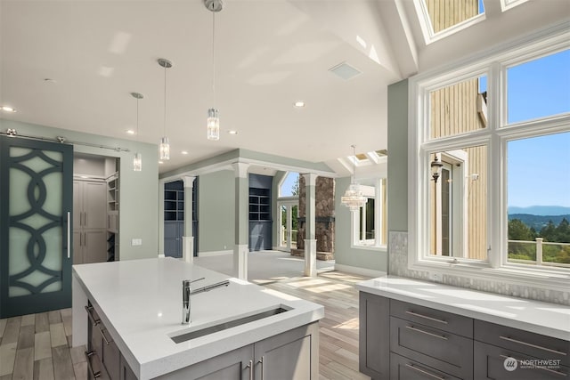 kitchen featuring a sink, a wealth of natural light, a center island, decorative columns, and pendant lighting