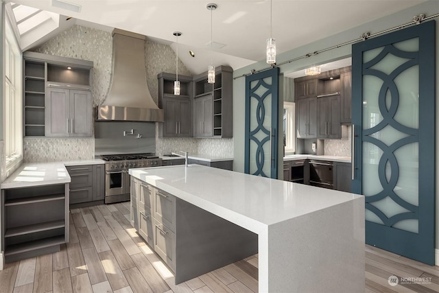 kitchen featuring a center island with sink, custom range hood, light countertops, double oven range, and open shelves