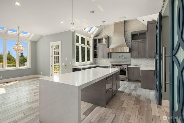 kitchen featuring decorative light fixtures, a spacious island, light countertops, high end stainless steel range oven, and wall chimney exhaust hood