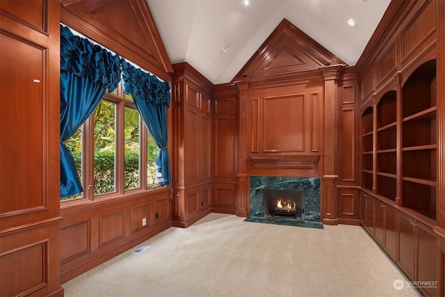 living area with light carpet, a decorative wall, vaulted ceiling, and a high end fireplace