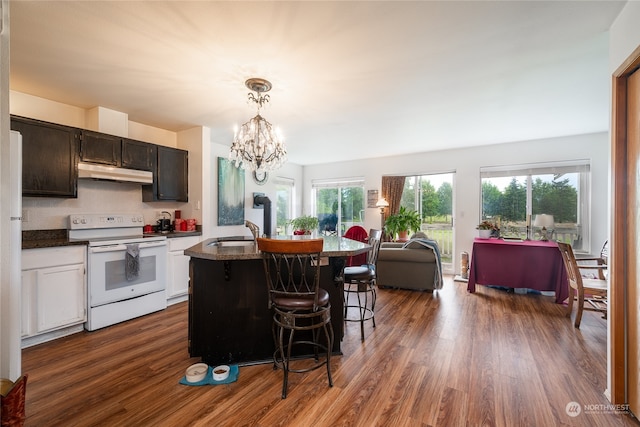 kitchen featuring an inviting chandelier, decorative light fixtures, electric range, dark hardwood / wood-style floors, and an island with sink