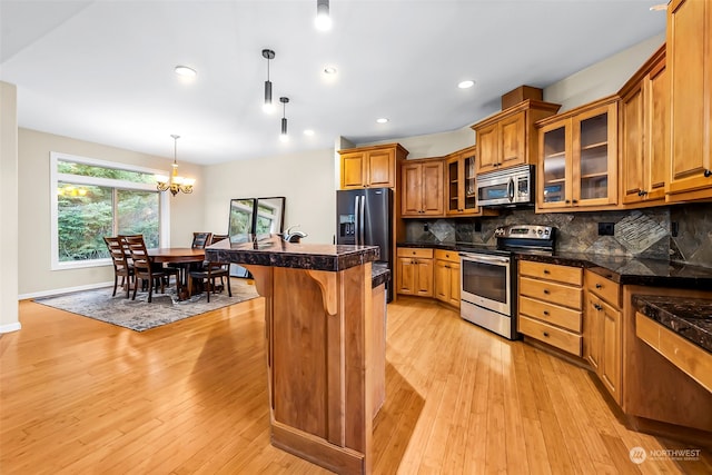 kitchen with backsplash, stainless steel appliances, light hardwood / wood-style flooring, and hanging light fixtures