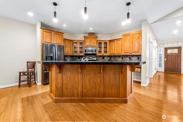 kitchen featuring tasteful backsplash, decorative light fixtures, a breakfast bar, appliances with stainless steel finishes, and light wood-type flooring