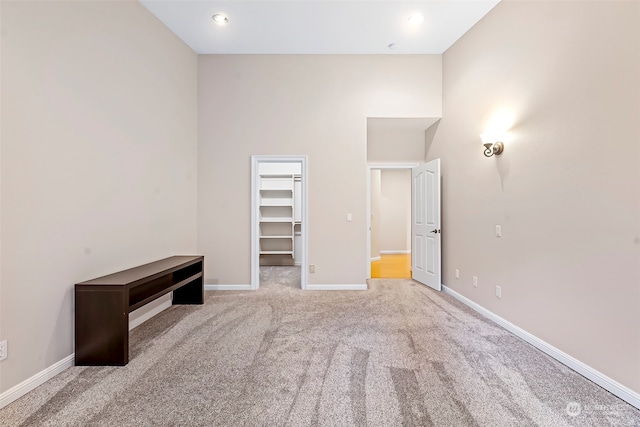 unfurnished bedroom with a walk in closet, a closet, a towering ceiling, and light colored carpet