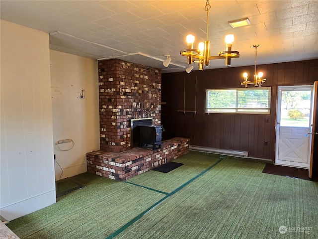 unfurnished living room with a notable chandelier, wooden walls, dark carpet, a wood stove, and a baseboard heating unit