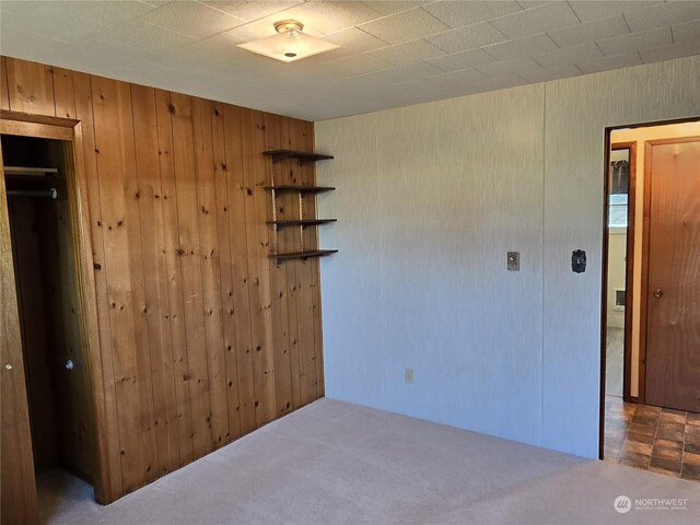 unfurnished bedroom with carpet, wood walls, and a closet