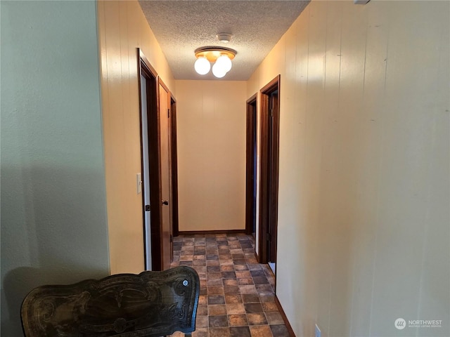 corridor featuring a textured ceiling, stone finish flooring, and baseboards