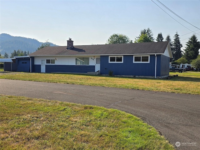 ranch-style house with a front yard, a chimney, and an attached garage