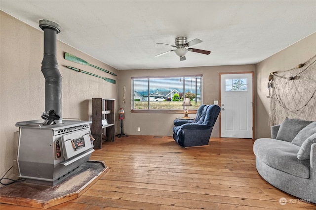 living room featuring light wood-style flooring, plenty of natural light, a wood stove, and a ceiling fan