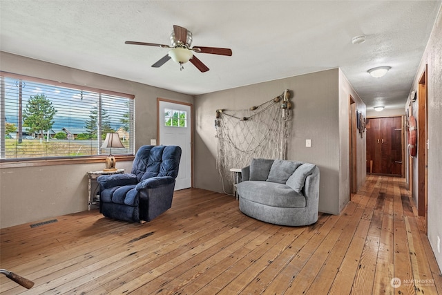 living area featuring ceiling fan, light wood-style flooring, a textured ceiling, and visible vents