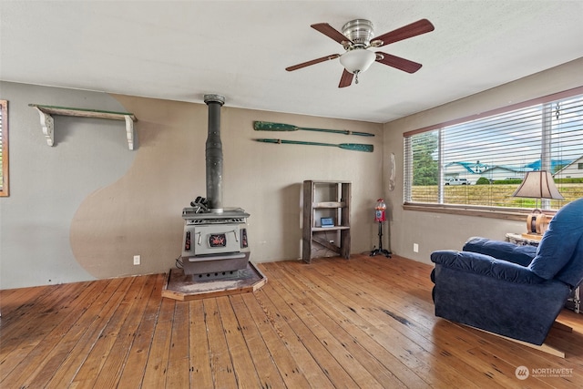 living room with a wood stove, wood-type flooring, and ceiling fan