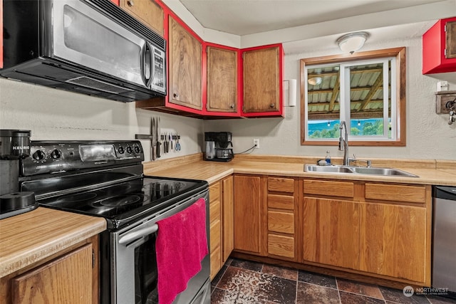 kitchen with stainless steel appliances, light countertops, a textured wall, stone finish flooring, and a sink