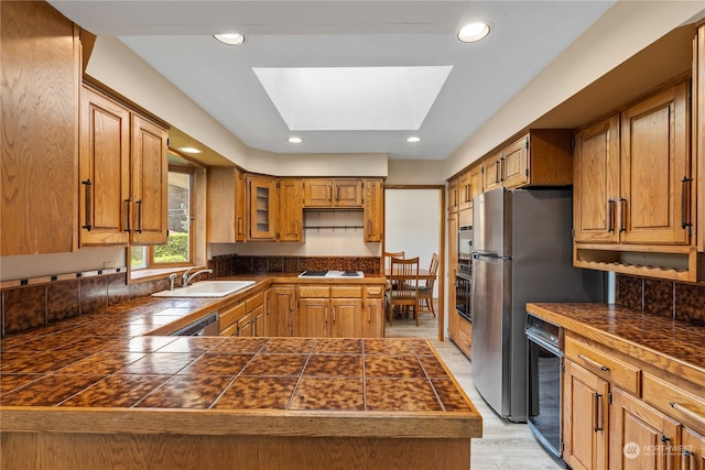 kitchen featuring light wood-type flooring, a skylight, kitchen peninsula, sink, and appliances with stainless steel finishes