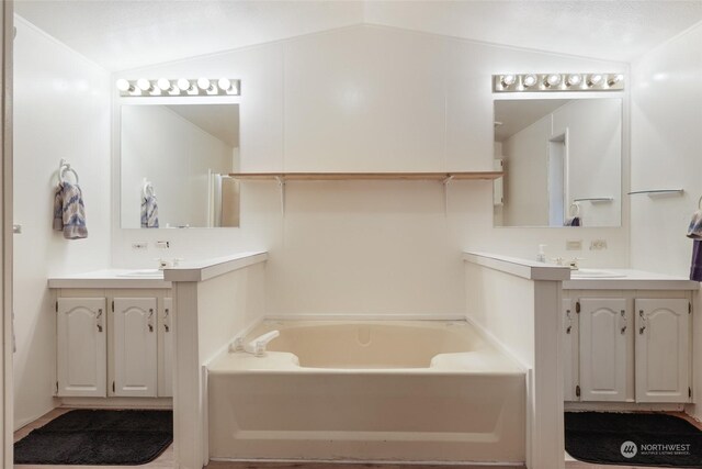 bathroom featuring a tub to relax in, vanity, and vaulted ceiling