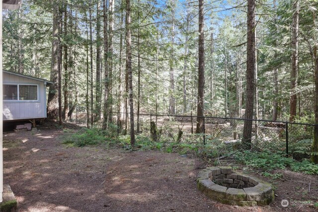 view of yard with a fire pit, fence, and a view of trees