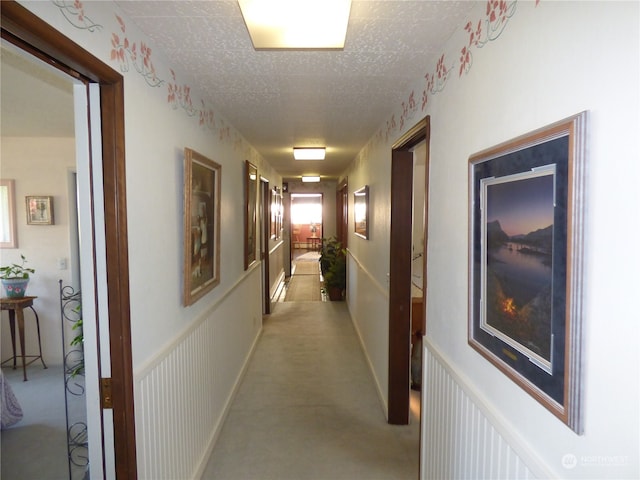 corridor with a textured ceiling and light carpet