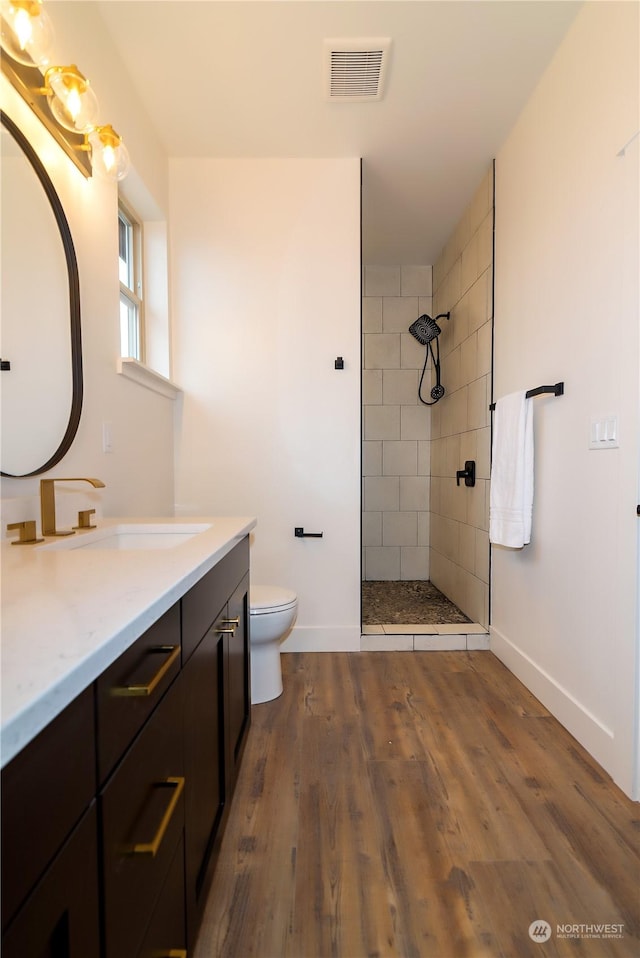 bathroom with a tile shower, vanity, wood-type flooring, and toilet