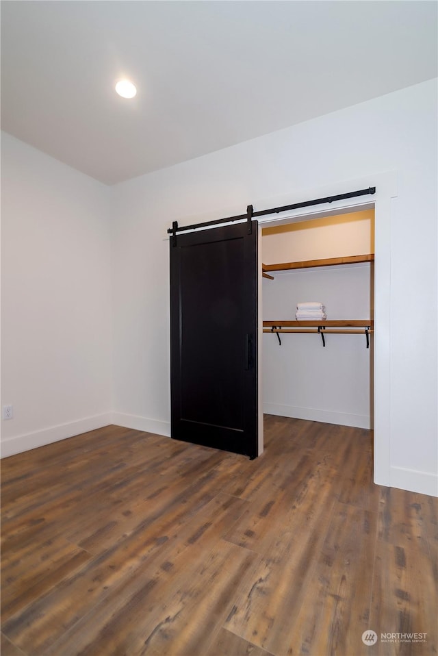 unfurnished bedroom with dark hardwood / wood-style flooring, a barn door, and a closet