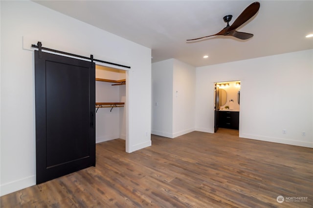 unfurnished bedroom with a barn door, dark hardwood / wood-style floors, ceiling fan, and connected bathroom