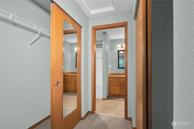 corridor with baseboards and light colored carpet